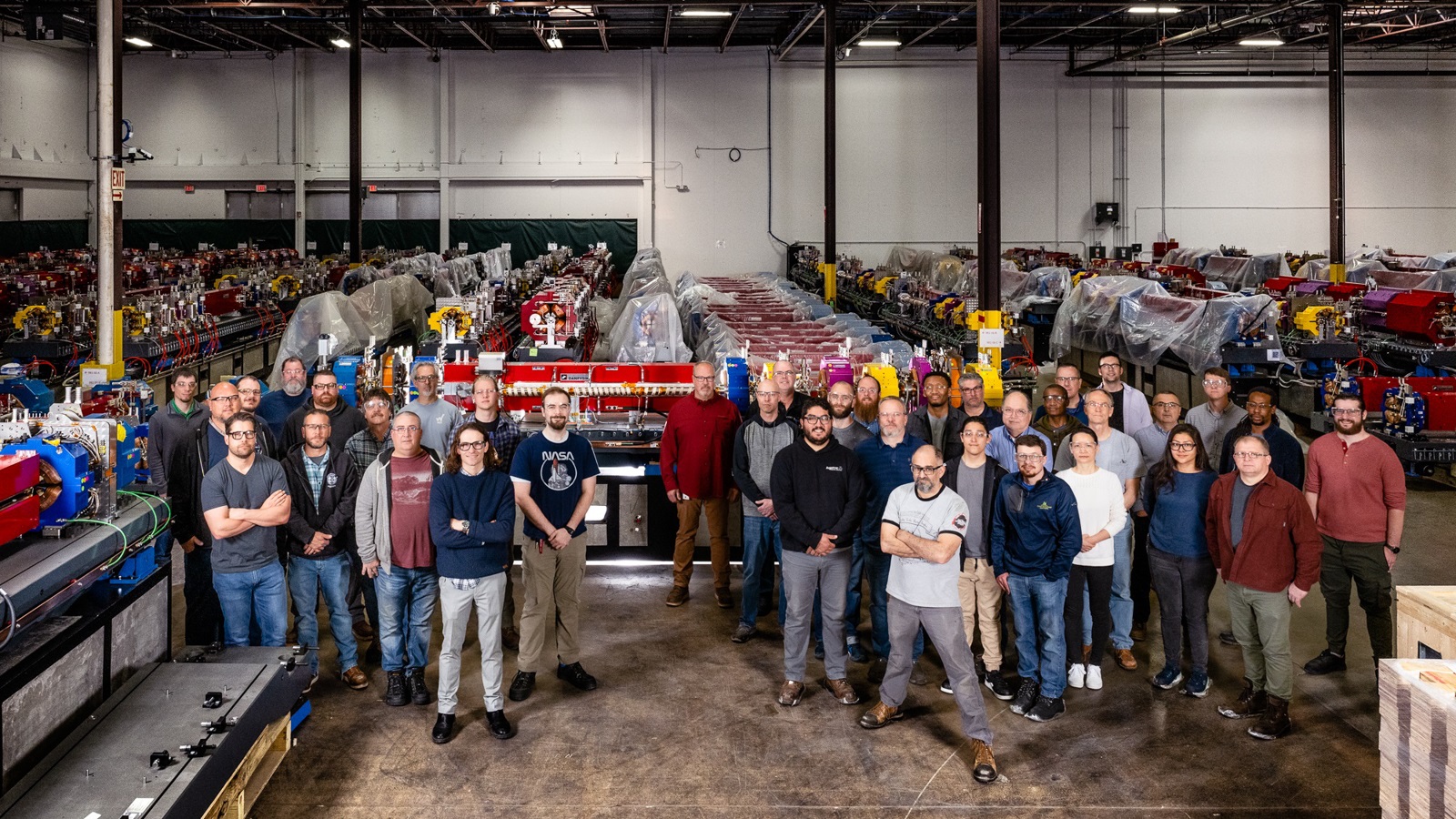 The APS Upgrade module assembly team surrounds the 100th completed module for the new APS storage ring. In the background are fully completed modules waiting for transport and installation. (Image by Argonne National Laboratory/Jason Creps.)